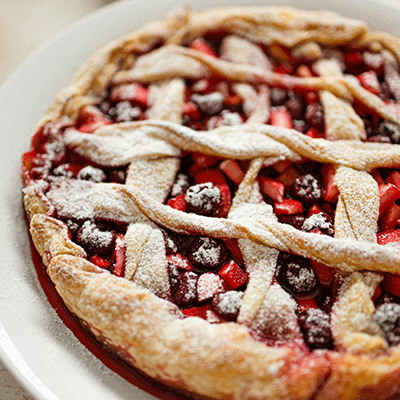 Closeup shot of large lattice pie with various berries filled inside.
